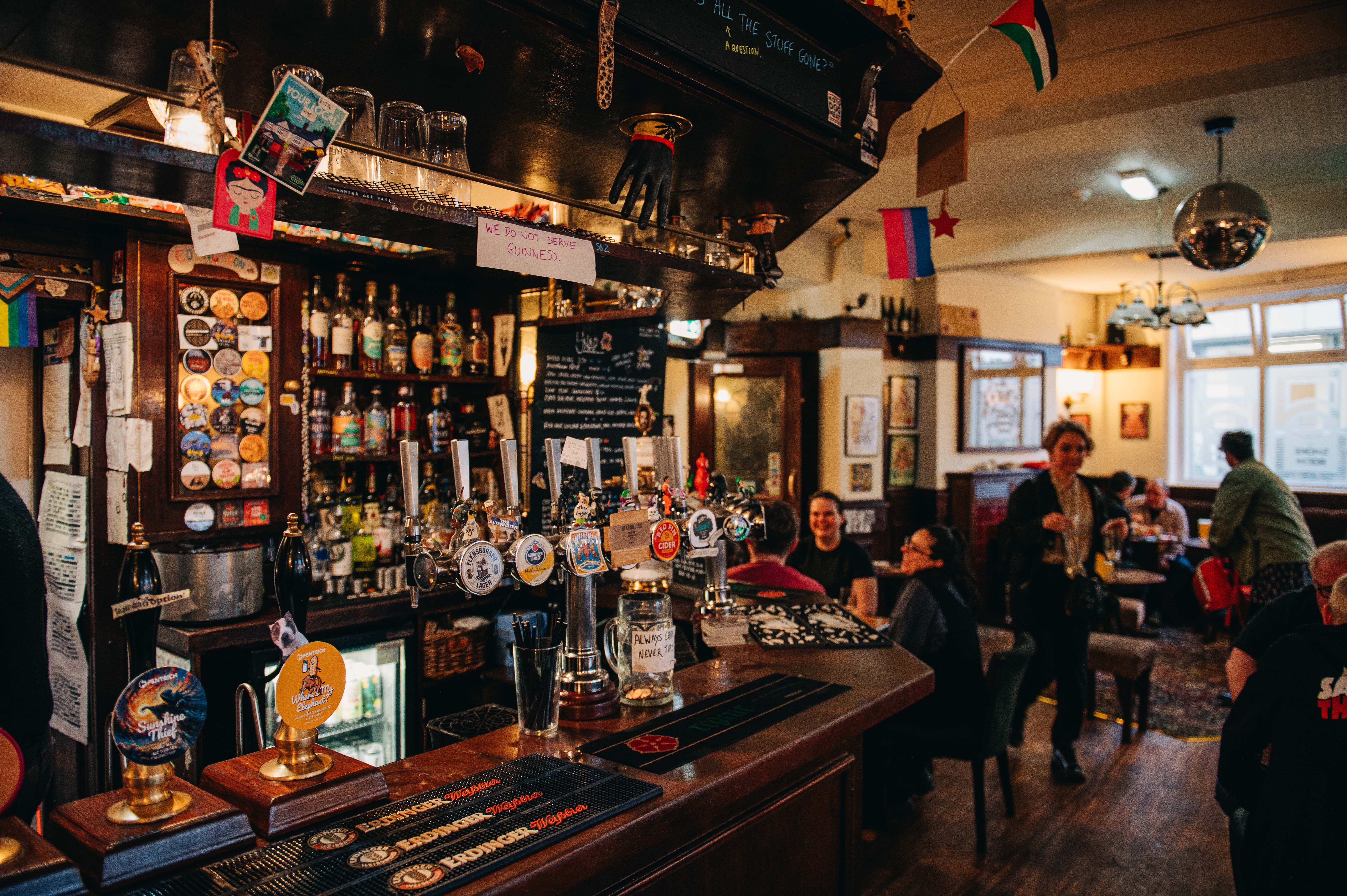 Rutland Arms interior. The bar is at the forefront, with groups of people in the background sat talking at drinking.