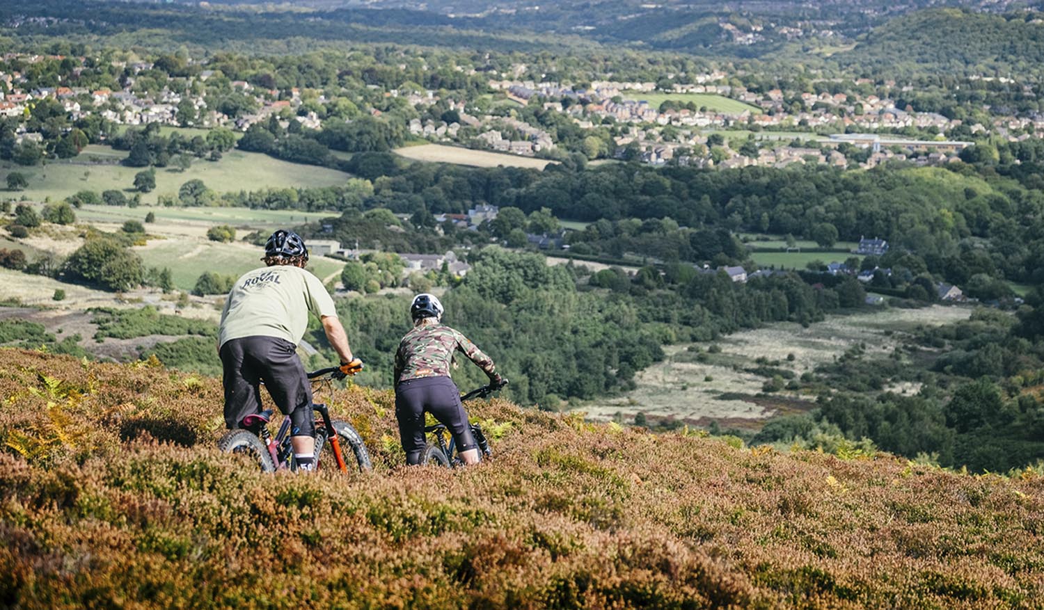 Two people mountain biking through the heather on a hillside above Sheffield.