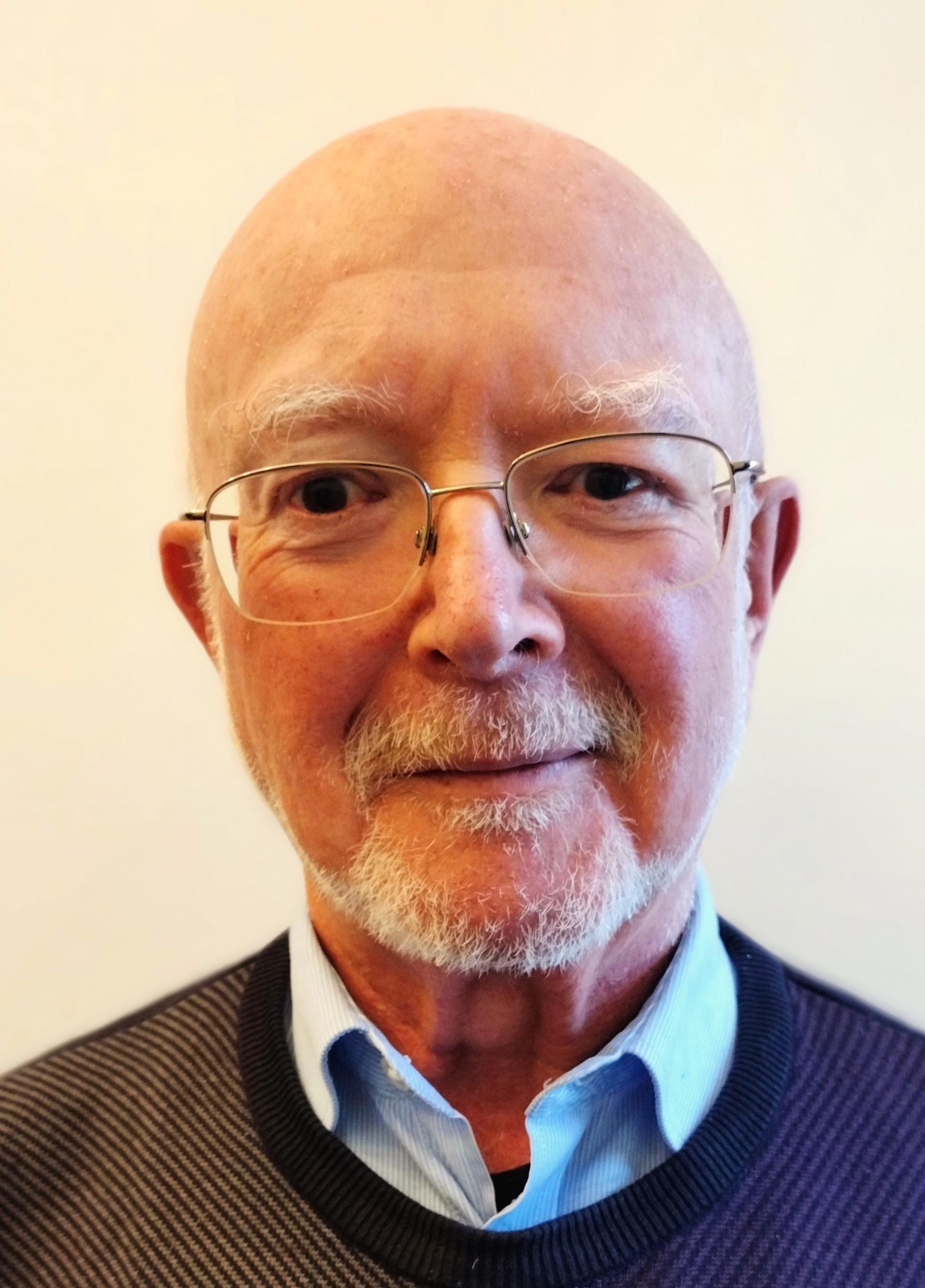 A head and shoulders portrait of a person, smiling at the camera against a plain, pale background.