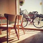 Simple but lovely wooden table and chairs at Amici & Bici. Outside a bike leans against the window.