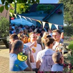 A busy outdoor gathering in a sunny courtyard, with people holding drinks and chatting under colourful bunting near a building and trees.