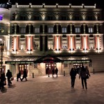 People walking through Tudor Square towards the Lyceum Theatre, at night.