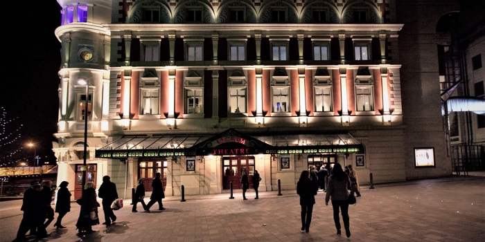 People walking through Tudor Square towards the Lyceum Theatre, at night.