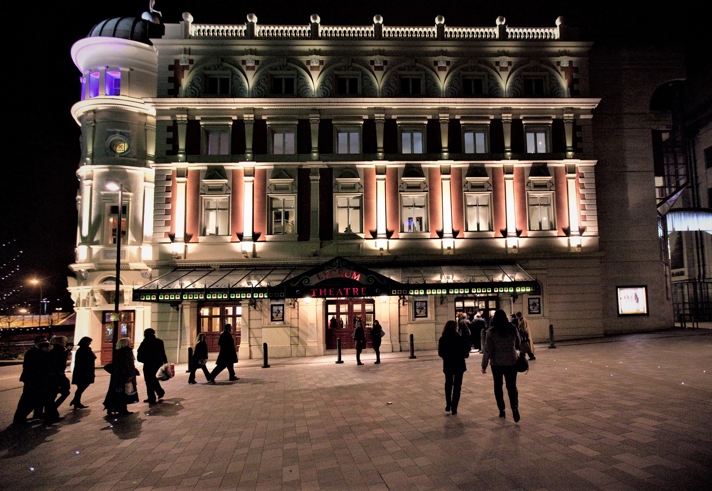 People walking through Tudor Square towards the Lyceum Theatre, at night.