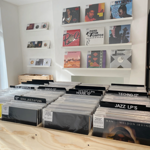 Inside a cosy record shop you can see racks of vinyl and records displayed on the wall. The shop decor is white and minimalist.