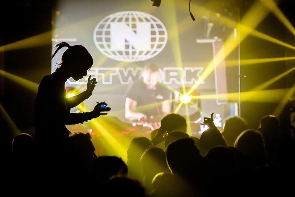 A nightclub full of people dancing, lit by yellow lighting.
