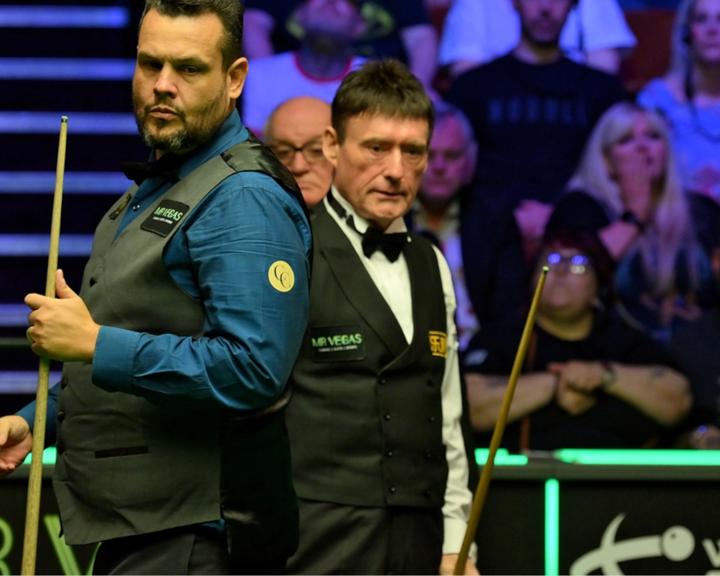 Two snooker players in the middle of a match at the Crucible. A crowd watches.