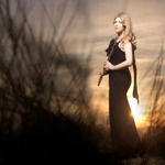 A woman in an evening dress stands in the countryside at sundown.