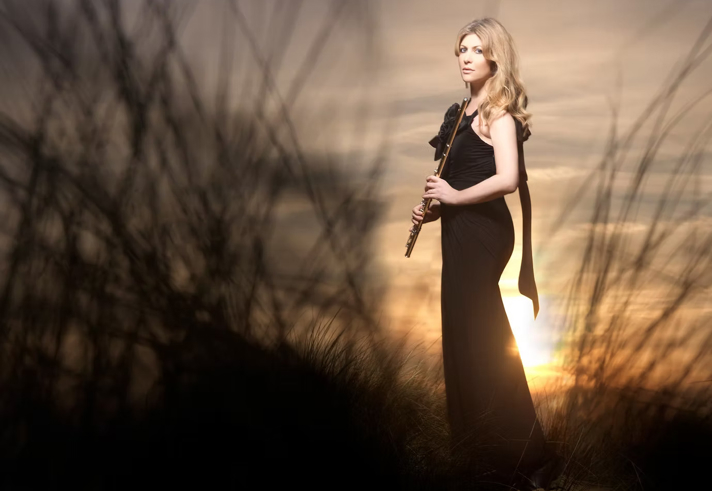A woman in an evening dress stands in the countryside at sundown.