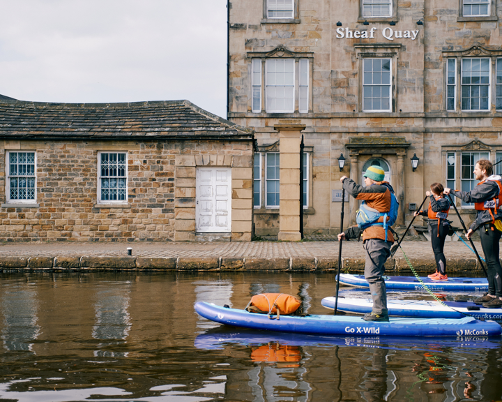 Three people stand up paddle boarding on a canal in Sheffield city centre.