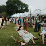 An outdoor event with lots of marquees, crowds of people walking about and some sitting in deck chairs.