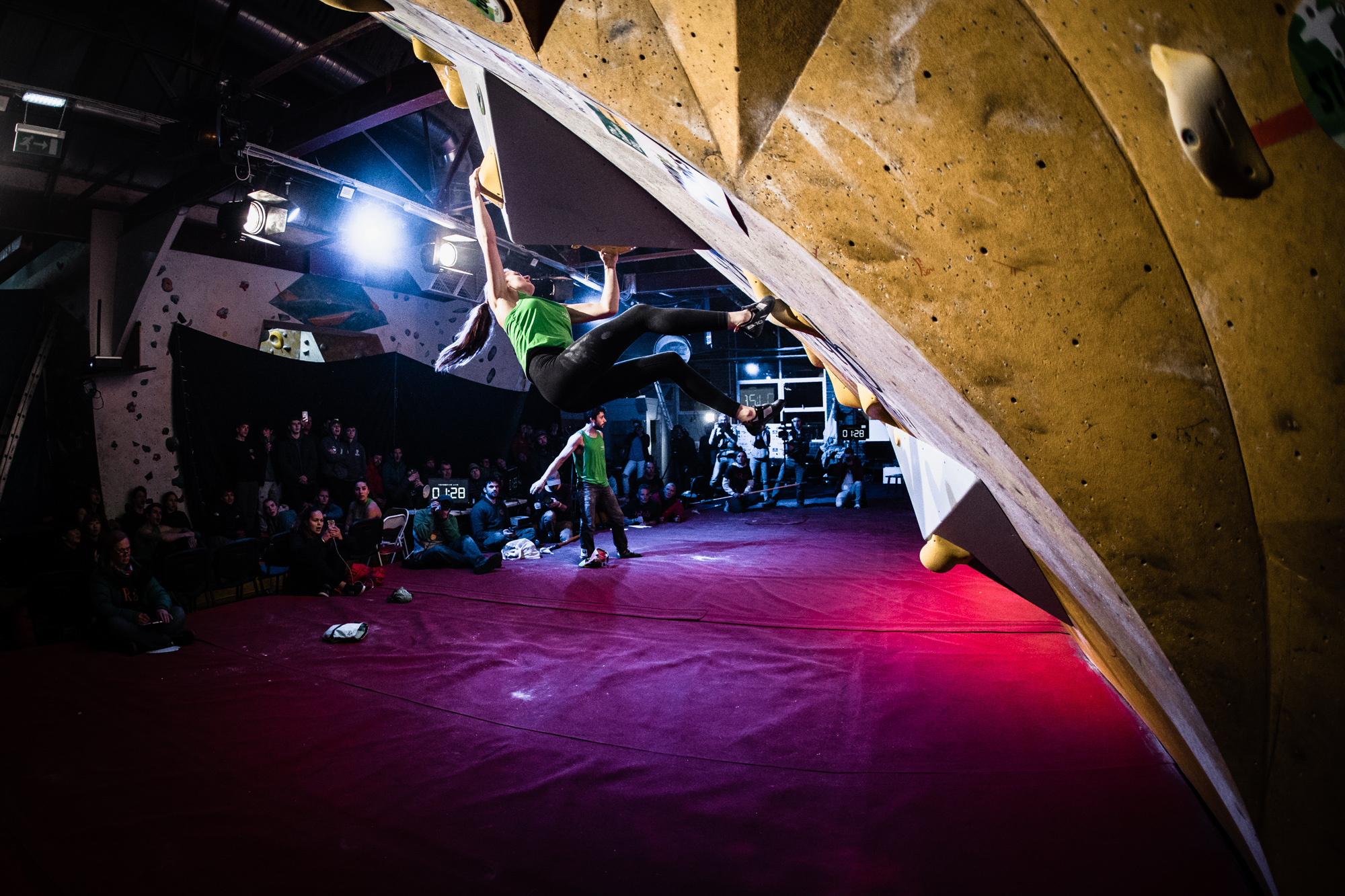 A woman is holding onto a climbing wall. She has two hands and one foot on the wall, with one foot mid-climb.