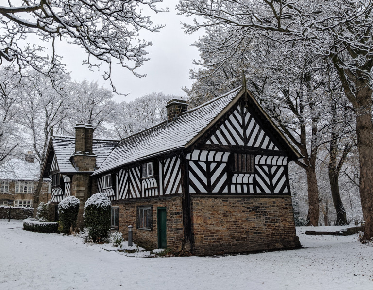 The Bishop's House in the snow. The bottom half of the building is stone and the top half is black and white timbers.