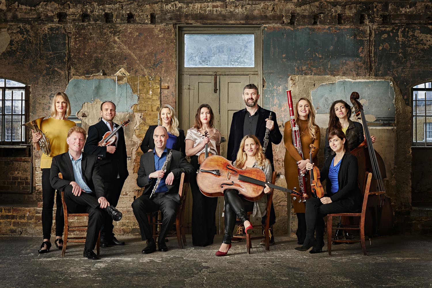 A portrait of Ensemble 360, all of whom are holding their instruments, in what appears to be a derelict building.