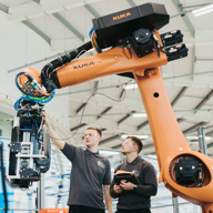 Two people are working on a large robot arm.