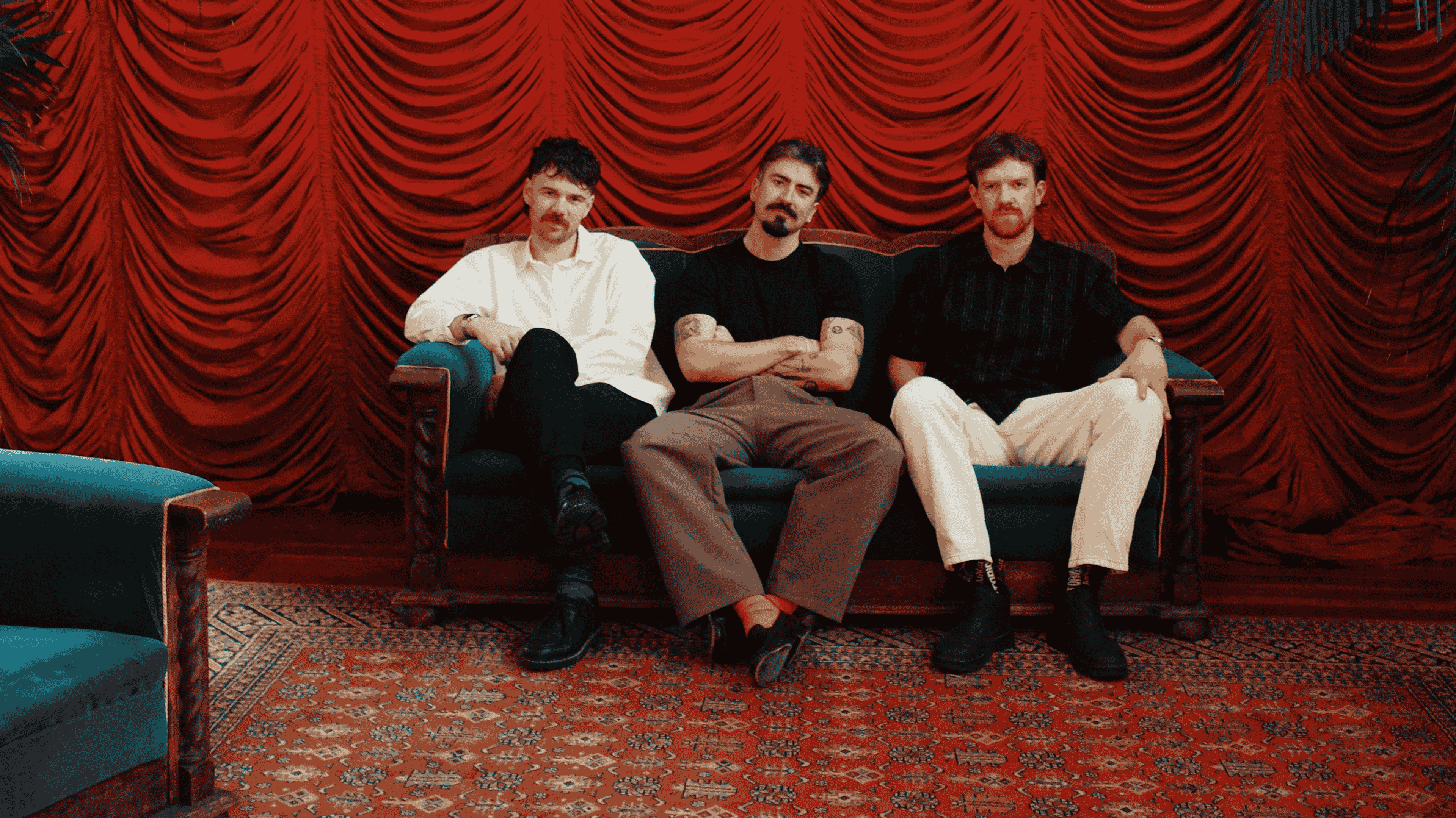 Three people sat on a sofa in front of a red pleated curtain.