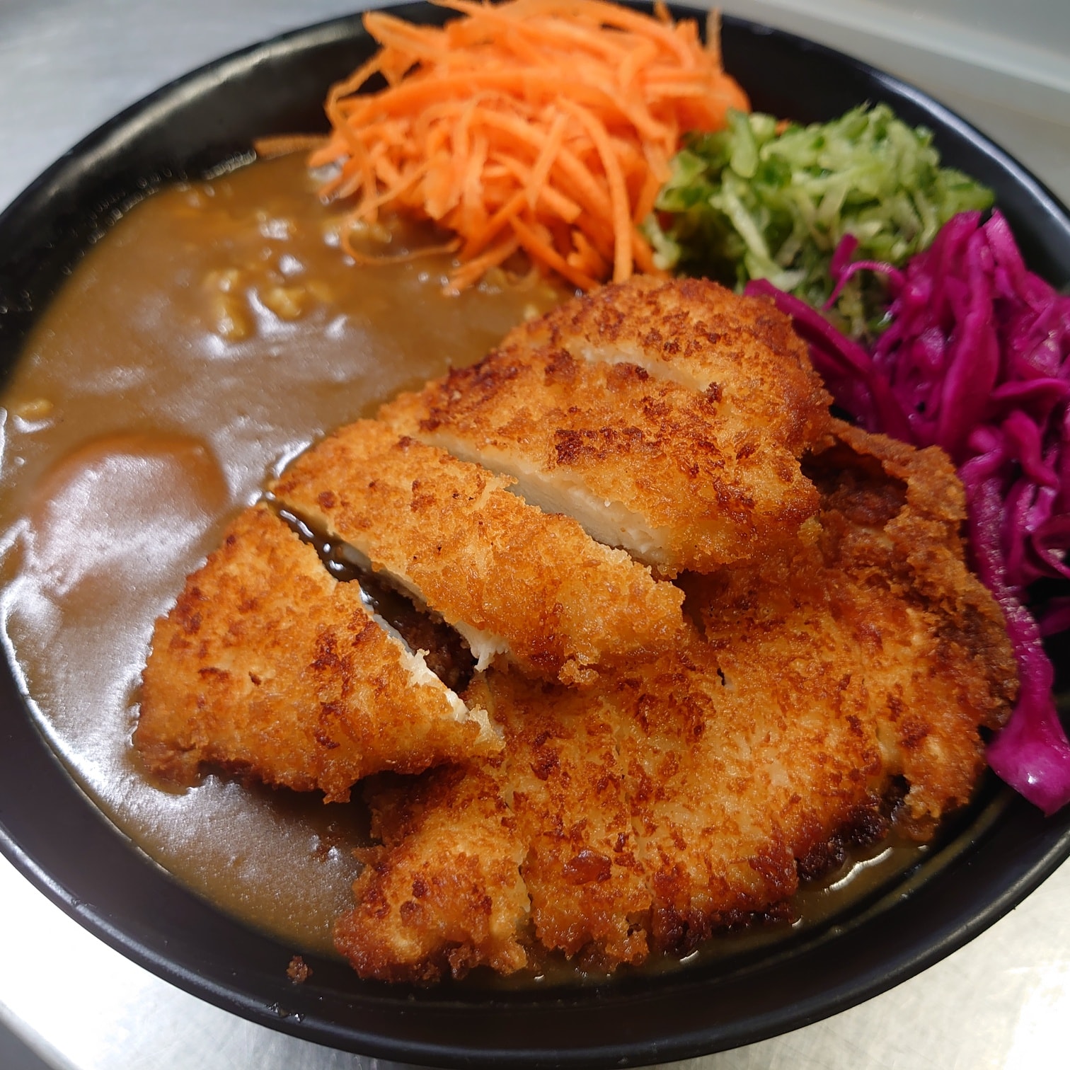 A plate of Japanese food , with breaded chicken, vegetables and a thick, brown sauce.