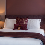 Elegant double bed with plush bedding and accent cushions in a cosy hotel room.