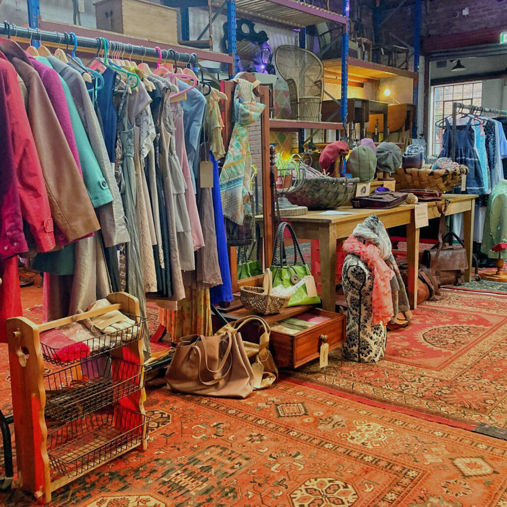 Inside The Warehouse with shelves and tables covered in things to buy and rails full of clothes.