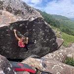 A woman climbing on a large rock. There is a thick safety mat on the ground below her.