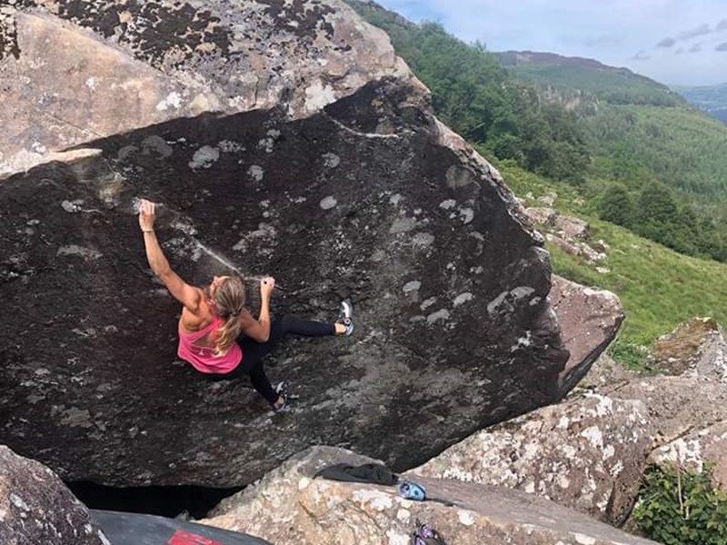 A woman climbing on a large rock. There is a thick safety mat on the ground below her.