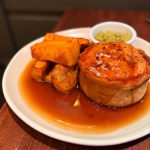 A plated pub meal consisting of a golden pie served with thick-cut roasted potatoes, gravy, and a small bowl of mushy peas.