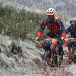 Two people cycling along a track in the countryside, in heavy rain.