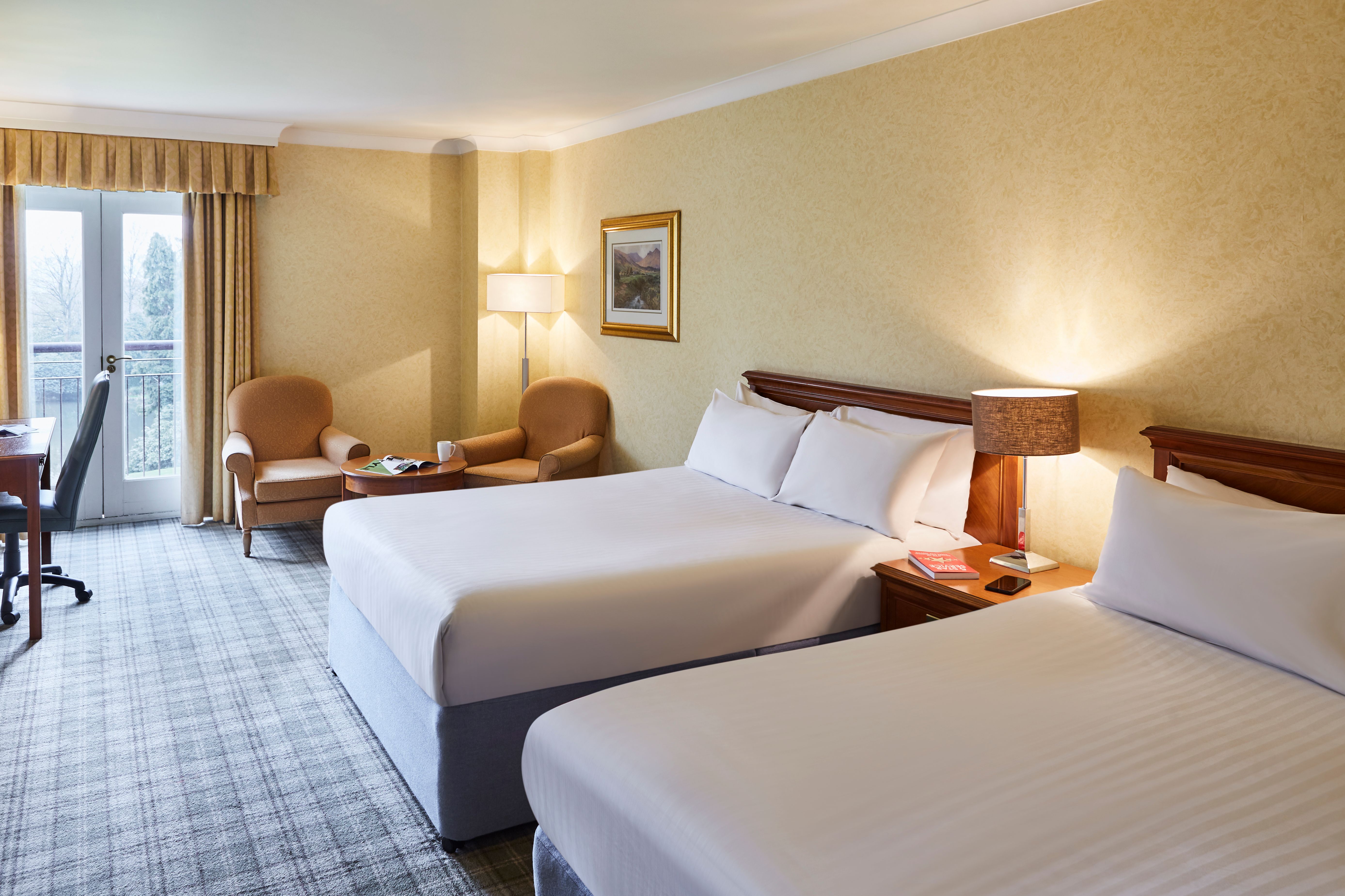 Bright, well-lit bedroom featuring two double beds with coordinated bedding and a cosy seating area near the window.