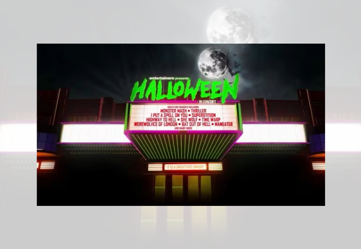 Stylised Halloween-themed graphic of a cinema or theatre marquee lit with neon green, pink and yellow lights at night. A large full moon and flying bats appear in the dark sky above. Bright green text reads “Halloween” while the marquee lists classic horror-themed songs including Monster Mash, Thriller, I Put a Spell on You, Superstition and Highway to Hell. The image has a retro horror and concert-poster aesthetic.