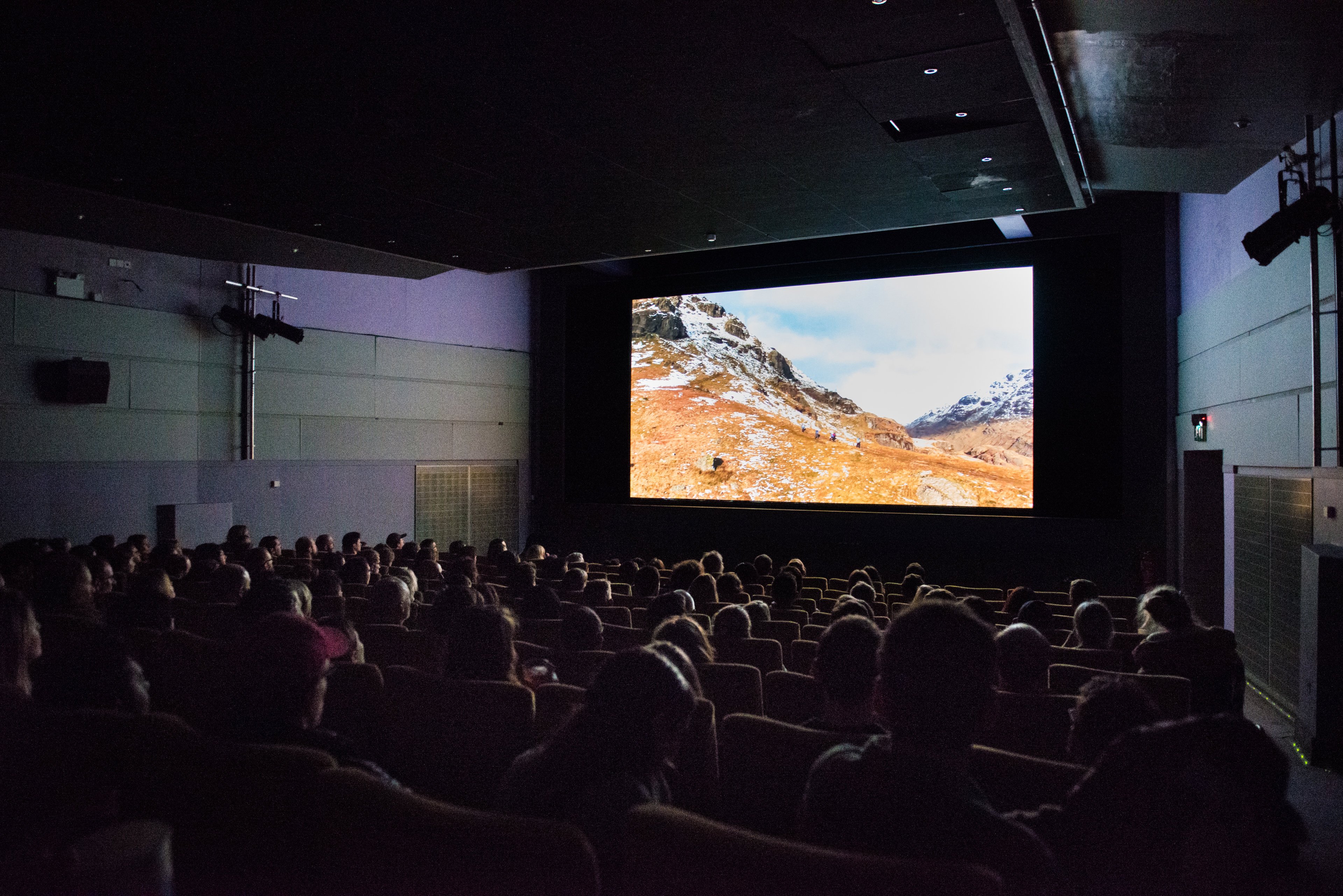Cinema room full of people, with a cinema screen showing a snowy mountain