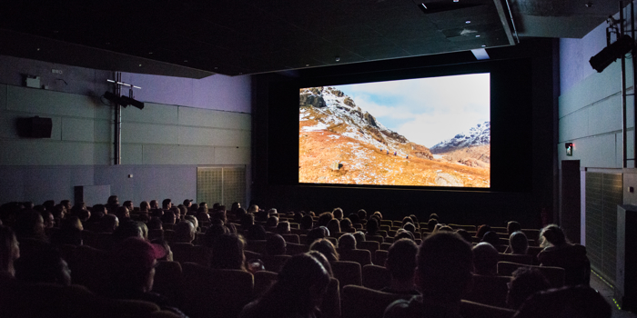 Cinema room full of people, with a cinema screen showing a snowy mountain
