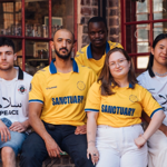 Members of the Theatre Company of Sanctuary pose outside a red brick building.