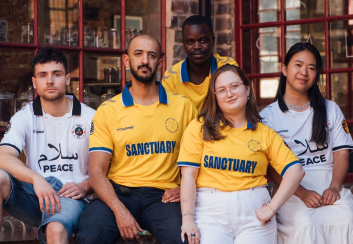 Members of the Theatre Company of Sanctuary pose outside a red brick building.
