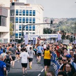 A group of people running towards the finish line of Sheffield Half Marathon in Castlegate on a sunny day. Spectators are cheering on from either side of the track.