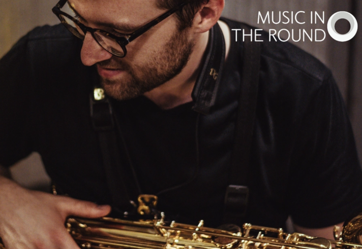 Close up of a man holding a saxophone in his lap.
