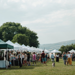 A row of marquee style tents at an outdoor event, with lots of people.