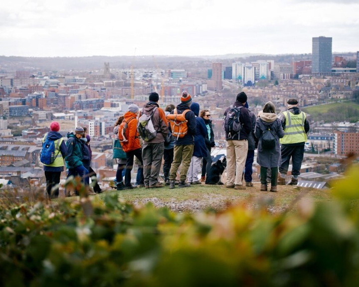 A group of walkers stand on top of a hill overlooking Sheffield city centre.