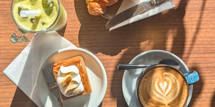 A wooden table, in the sun, with a coffee, delicious pastries and a smoothie at the Copper Pot Café.