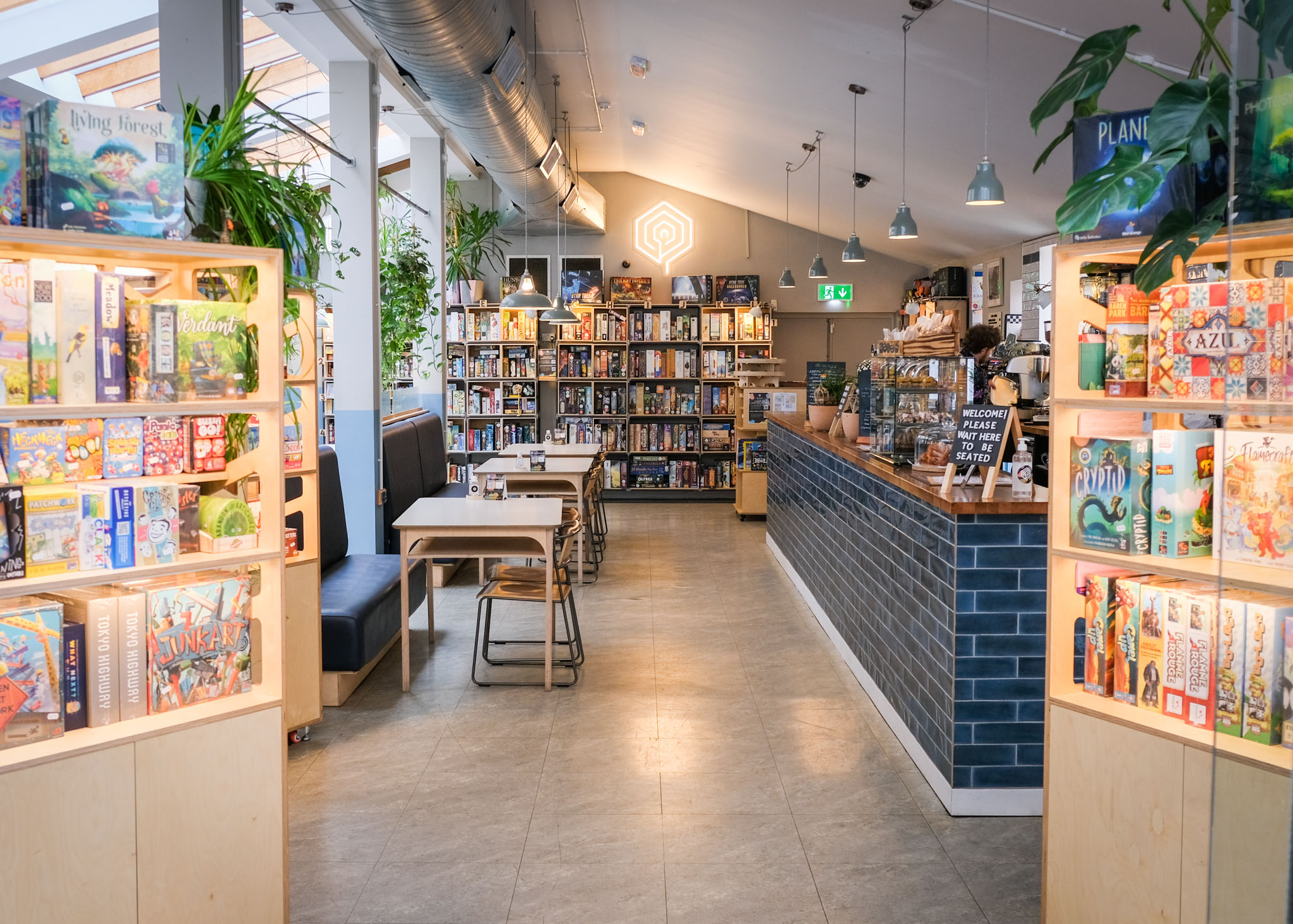 Inside The Treehouse Cafe. You can see tables and chairs, the counter and three shelving units full of board games.