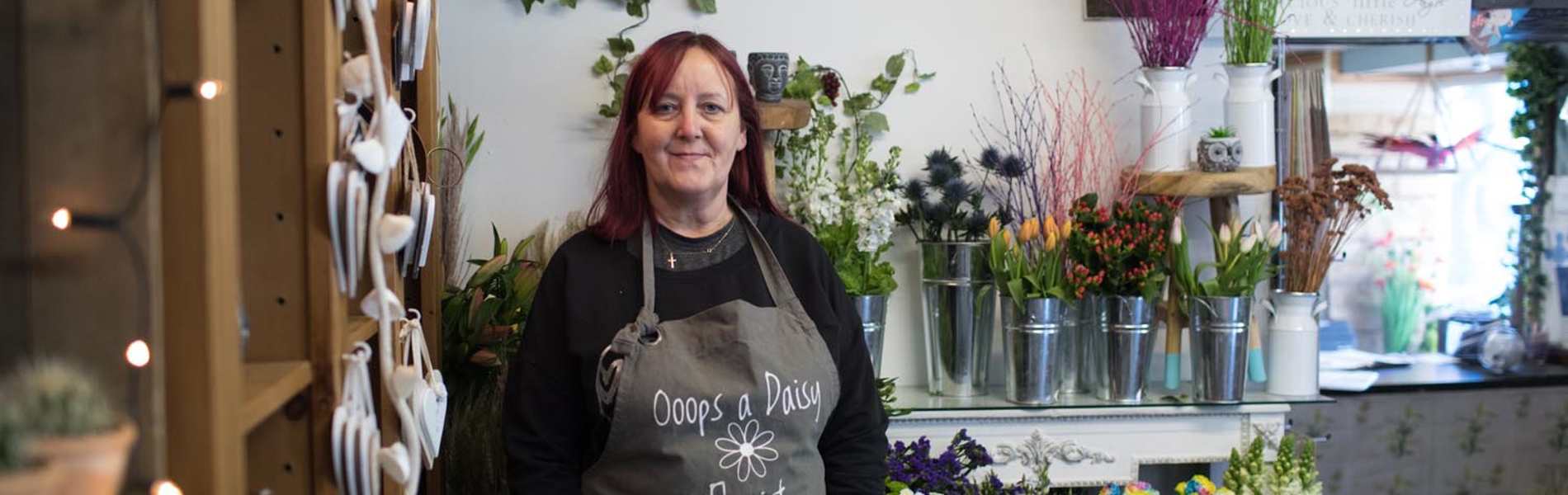 A Sheffield florist stands in front of rows of many vases of flowers of all colours.