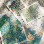 Four botanical art prints arranged on a light fabric surface with dappled sunlight. The prints depict lush greenery, tropical plants, and floral compositions in vivid colors, including one featuring a garden scene with a door and another showing rooftops and foliage.