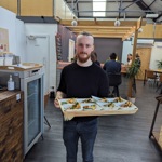 A man carrying a large tray with 8 plates of food in a restaurant.