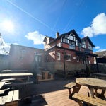 A sunlit outdoor decking area behind The Punch Bowl, with wooden picnic tables and string lights, and the pub building visible in the background.