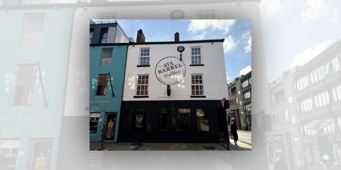 Street-level view of the Six Barrel Drafthouse, a white two-storey building with black trim and sash windows. A large circular sign on the front reads “Six Barrel Drafthouse” with “Cask Ales, Craft Beer, Fresh Coffee” around the edge. The ground floor has dark-painted shopfront windows displaying the words “Craft”, “Coffee” and “Cask”. A turquoise Mirage Vape Store is attached on the left, with modern city buildings and a Give Way sign visible on the right under a bright, partly cloudy sky.
