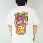 A man stands with his back to the camera, wearing a baseball bat, a white t-shirt with a colourful back print and green trousers. The design on the shirt is four anthropomorphic fruits busting out of a jam jar. They look like members of a band. The yellow label on the jar reads 'We're jammin''.