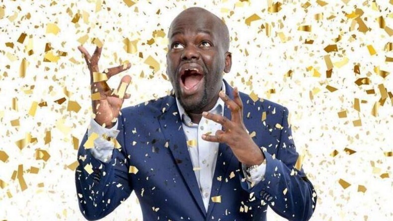 A person in a dark blue suit stands surrounded by falling gold confetti, with hands raised as if celebrating. The background is filled with shimmering gold pieces, creating a festive, energetic atmosphere.
