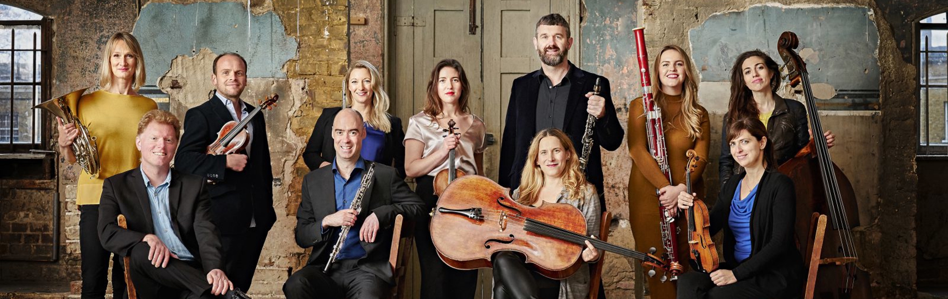 The members of Ensemble 360 pose in a dilapidated building. They are all smartly dressed and holding their instruments. 