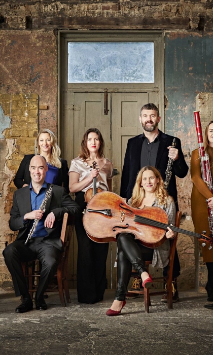The members of Ensemble 360 pose in a dilapidated building. They are all smartly dressed and holding their instruments. 