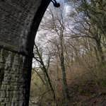 A tall stone arch of a bridge over a river. A person is abseiling down the side.