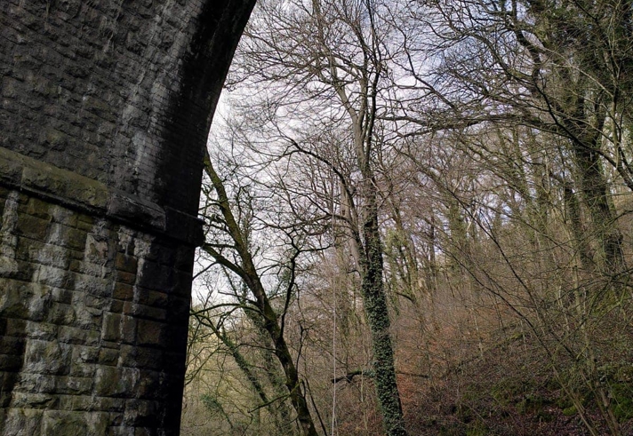 A tall stone arch of a bridge over a river. A person is abseiling down the side.